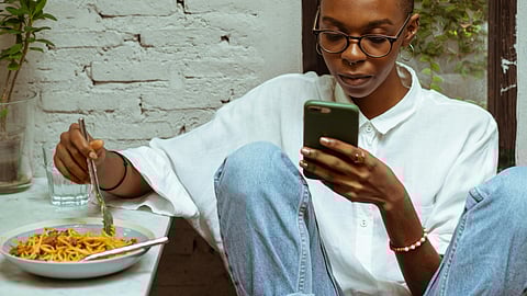 Focused black woman having lunch and browsing smartphone