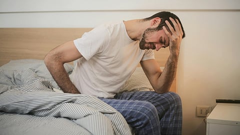 Young man in sleepwear suffering from headache in morning