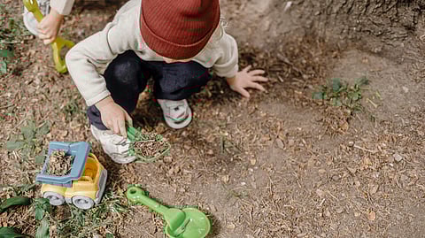 Little kid playing with plastic shovel and car in yard