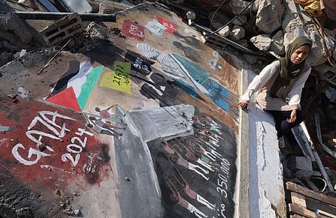 ഗാസ മുനമ്പിന്റെ തെക്ക് ഭാഗത്തുള്ള റഫയില് ഇസ്രയേല് ബോംബാക്രമണത്തിനിടെ തകര്ന്ന വീടിന്റെ ചുമരില് പലസ്തീനിയന് കലാകാരി അമല് ആബോ തന്റെ ചുവര്ചിത്രത്തിന് സമീപം ഇരിക്കുന്നു/ ഫോട്ടോ: എഎഫ്പി