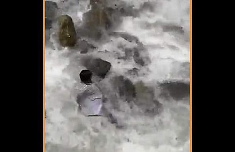 ഒഴുക്കില്പ്പെടാതിരിക്കാന് തീര്ഥാടകന് പാറയില് പിടിച്ചു കിടക്കുന്ന ദൃശ്യം