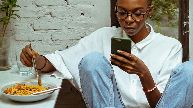 Focused black woman having lunch and browsing smartphone