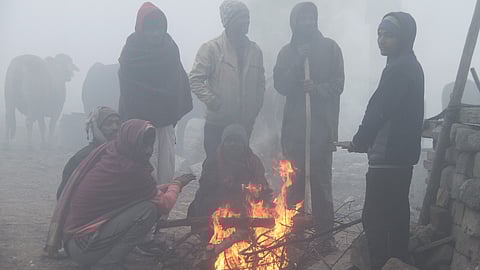 People gather around the bonfire to keep themselves warm on a cold winter morning, in Gurugram 