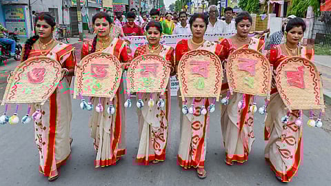 Women wearing traditional Bengali-styled saris hold 'Kulos' 