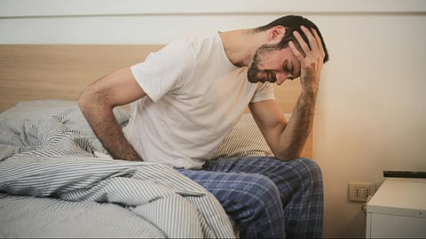 Young man in sleepwear suffering from headache in morning