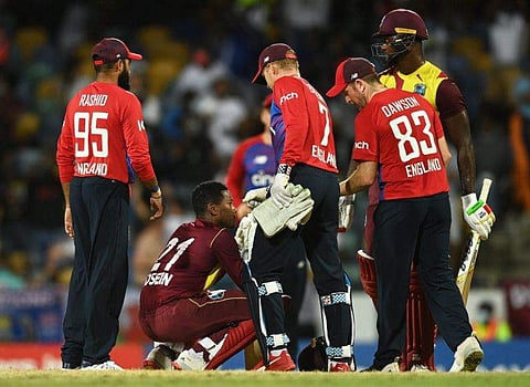 പൊരുതി തോറ്റതിന്റെ നിരാശയിൽ ക്രീസിൽ ഇരിക്കുന്ന അകീൽ ​ഹുസൈനെ ആശ്വസിപ്പിക്കുന്ന ഇം​ഗ്ലണ്ട് താരങ്ങൾ/ ട്വിറ്റർ