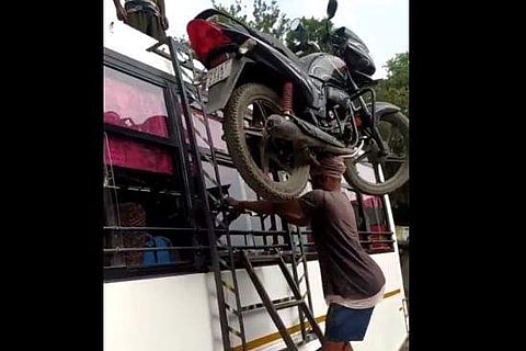 ബൈക്ക് തലച്ചുമടായി ബസിന്റെ മുകളിലേക്ക് കയറ്റുന്ന തൊഴിലാളിയുടെ ദൃശ്യം